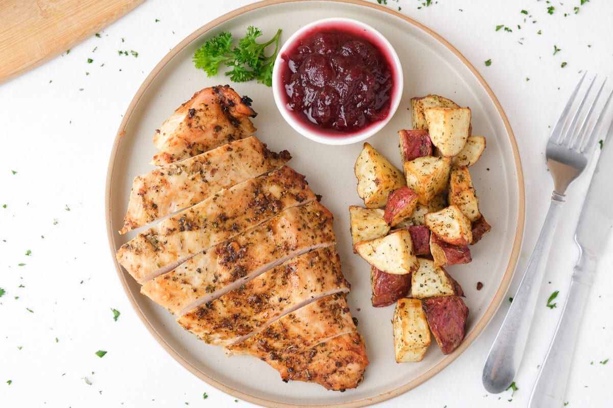 sliced cooked turkey breast on plate with potatoes and cranberries.