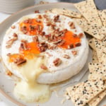 baked brie on plate with nuts and jelly on top with pita chips beside.