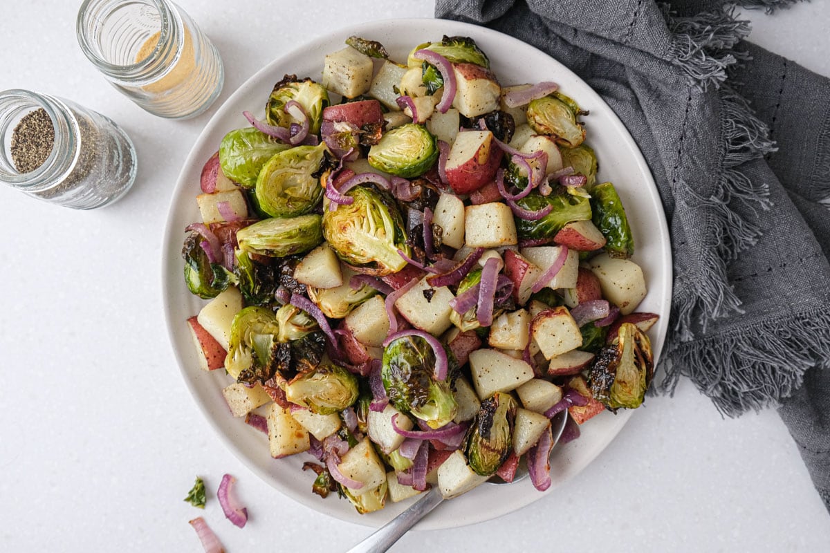 plate heaping with brussels sprouts and potatoes with grey cloth beside on counter.