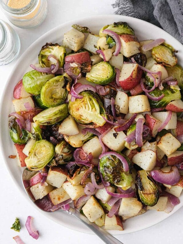 plate of brussels sprouts and potatoes with silver spoon on the edge sitting on white counter top.