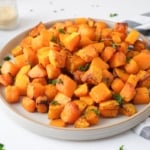 round grey plate of cooked butternut squash on counter top with dish cloth and spices beside.
