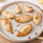 soft pears covered in chopped nuts on beige plate on wooden tray with more chopped nuts around.