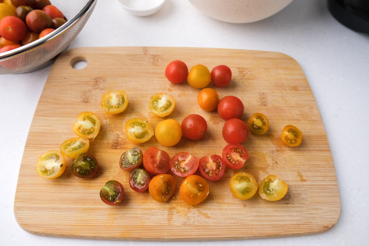 colorful cherry tomatoes cut in half on wooden cutting board on white counter.