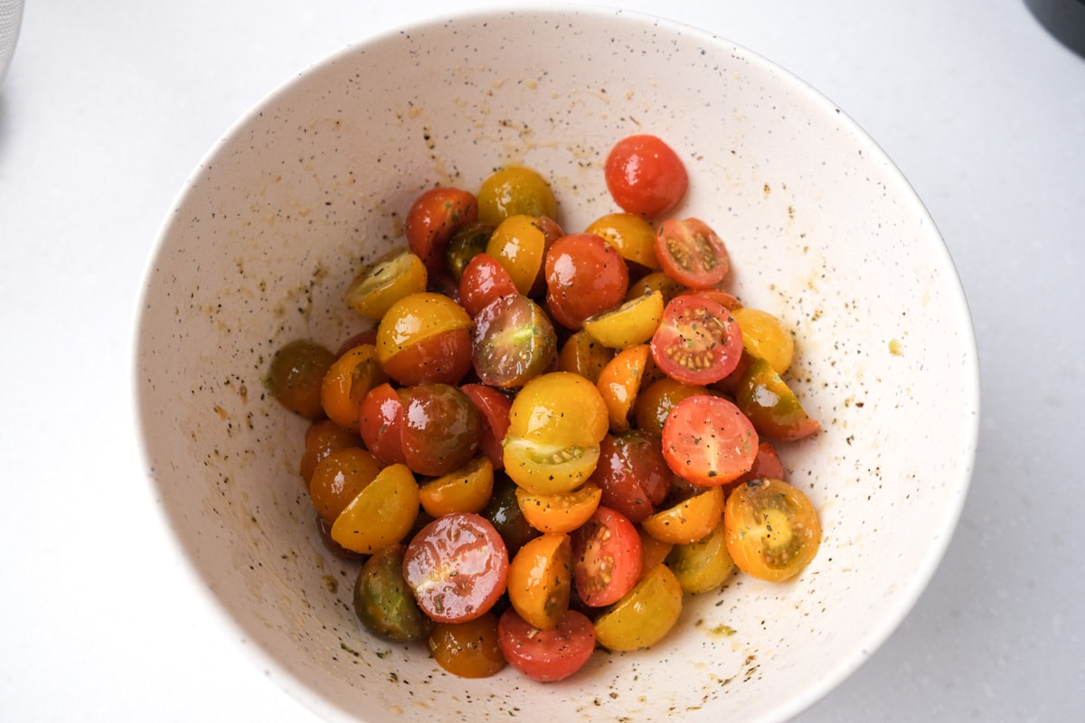 cherry tomatoes cut in half in white mixing bowl covered in oil and spices.