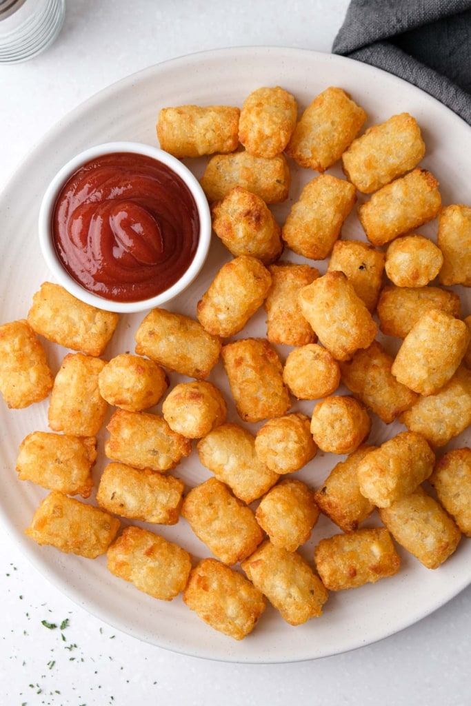 crispy golden tater tots on white plate with ketchup beside.