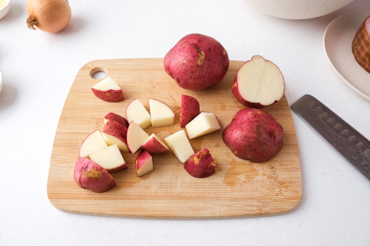 red potato cut into cubes on wooden cutting board on white counter top.