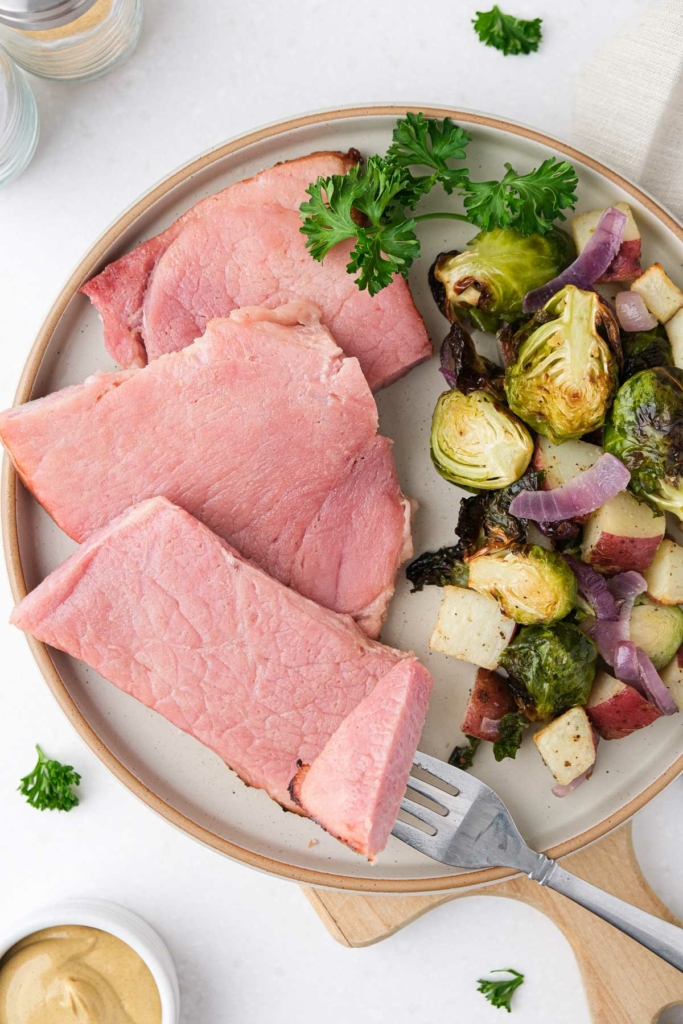 slices of ham on plate beside brussels sprouts and potatoes.