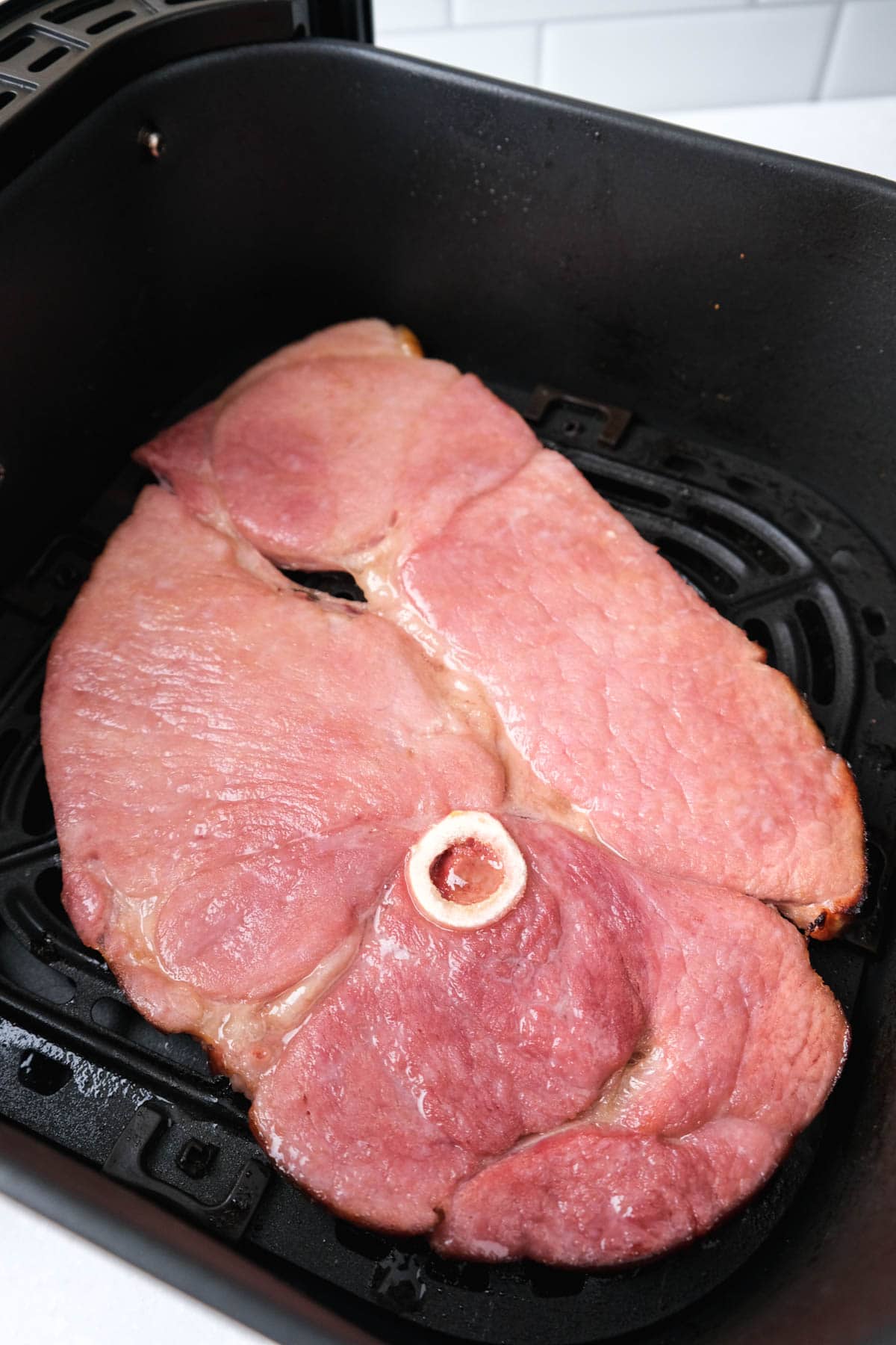 air fried ham steak sitting in black air fryer basket on white counter top.