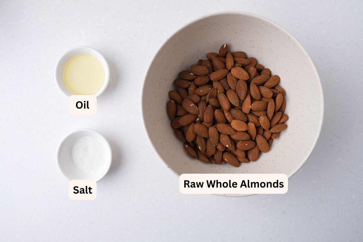 large bowl of almonds with other bowls of oil and salt on white counter top with labels.
