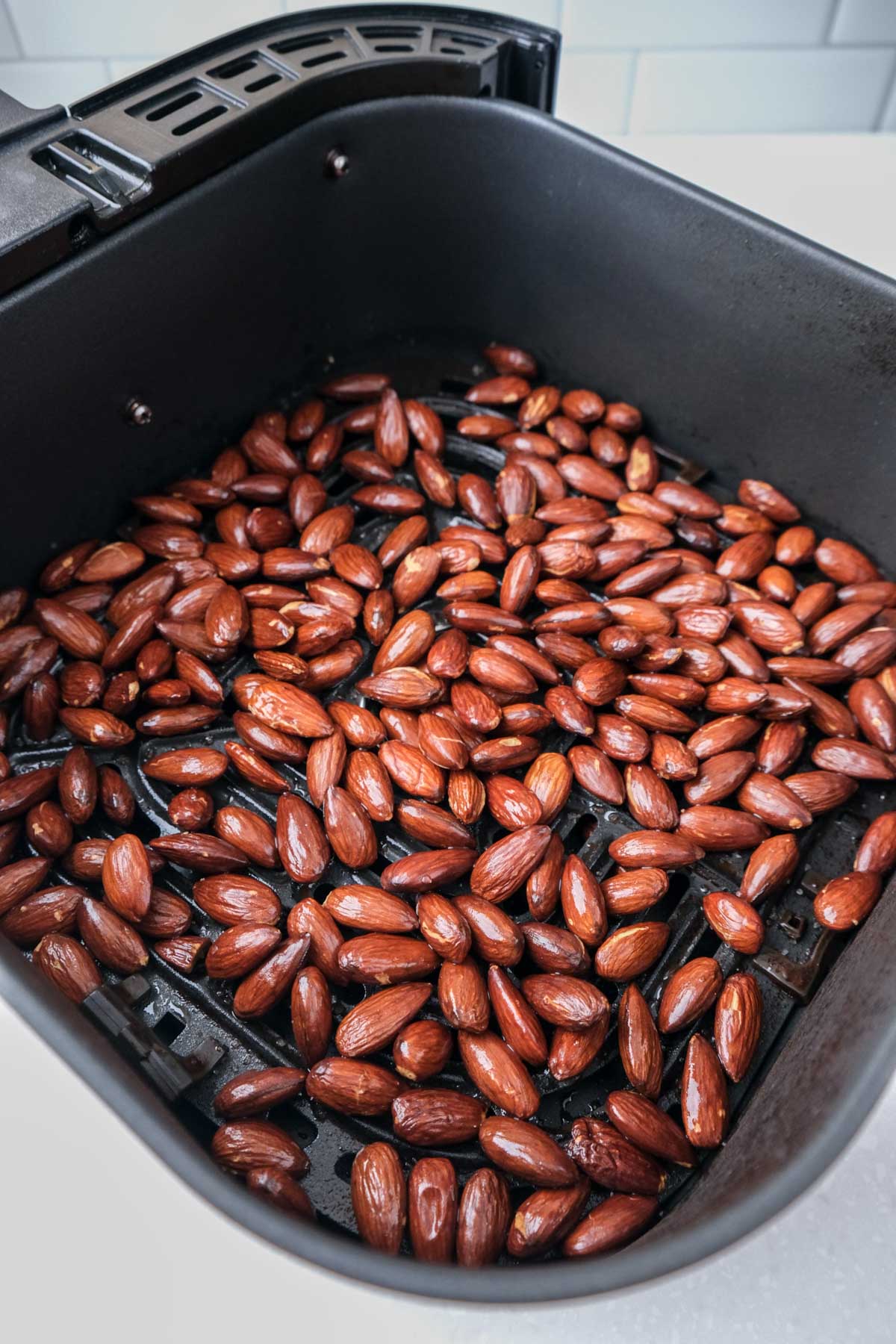 dark roasted almonds sitting in black air fryer tray on white kitchen counter.
