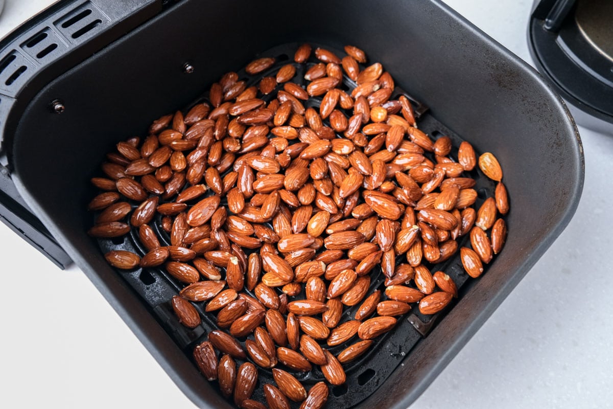 raw almonds sitting in black air fryer basket on white counter top.