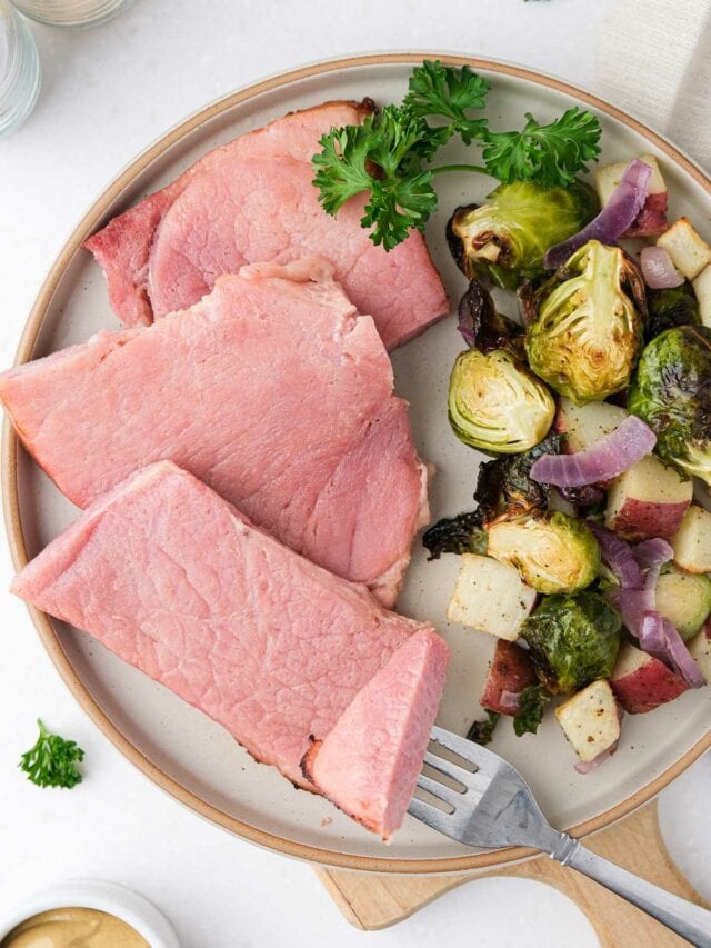 slices of ham on plate beside brussels sprouts and potatoes.