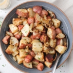 blue bowl with cubes of roasted ham and potatoes with silver spoon beside.