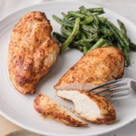 sliced cooked chicken breast displayed on plate with beans behind and silver fork in front.