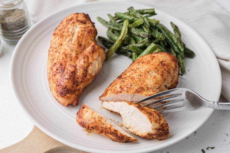 sliced cooked chicken breast displayed on plate with beans behind and silver fork in front.