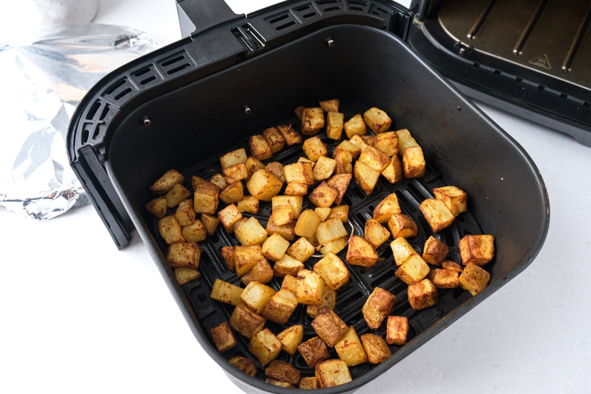 cooked potatoes in black air fryer tray on counter with tin foil behind.