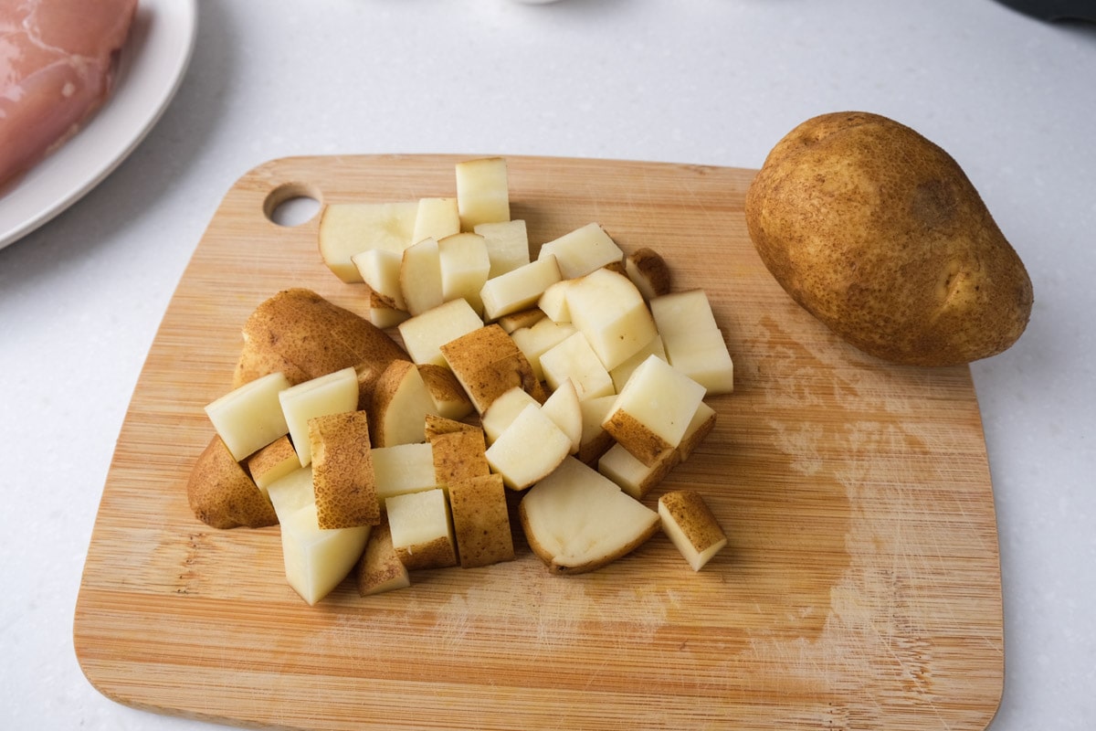 potatoes cut up on wooden cutting board with whole potato beside on counter.