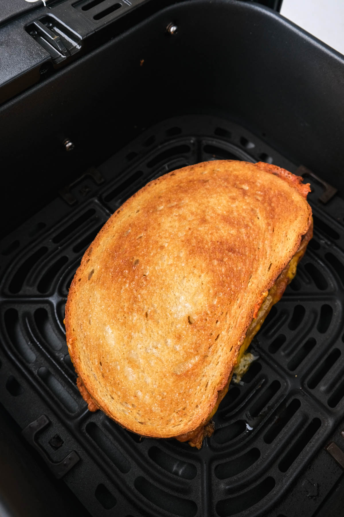 crispy grilled cheese with tomato in black air fryer tray sitting on white counter.