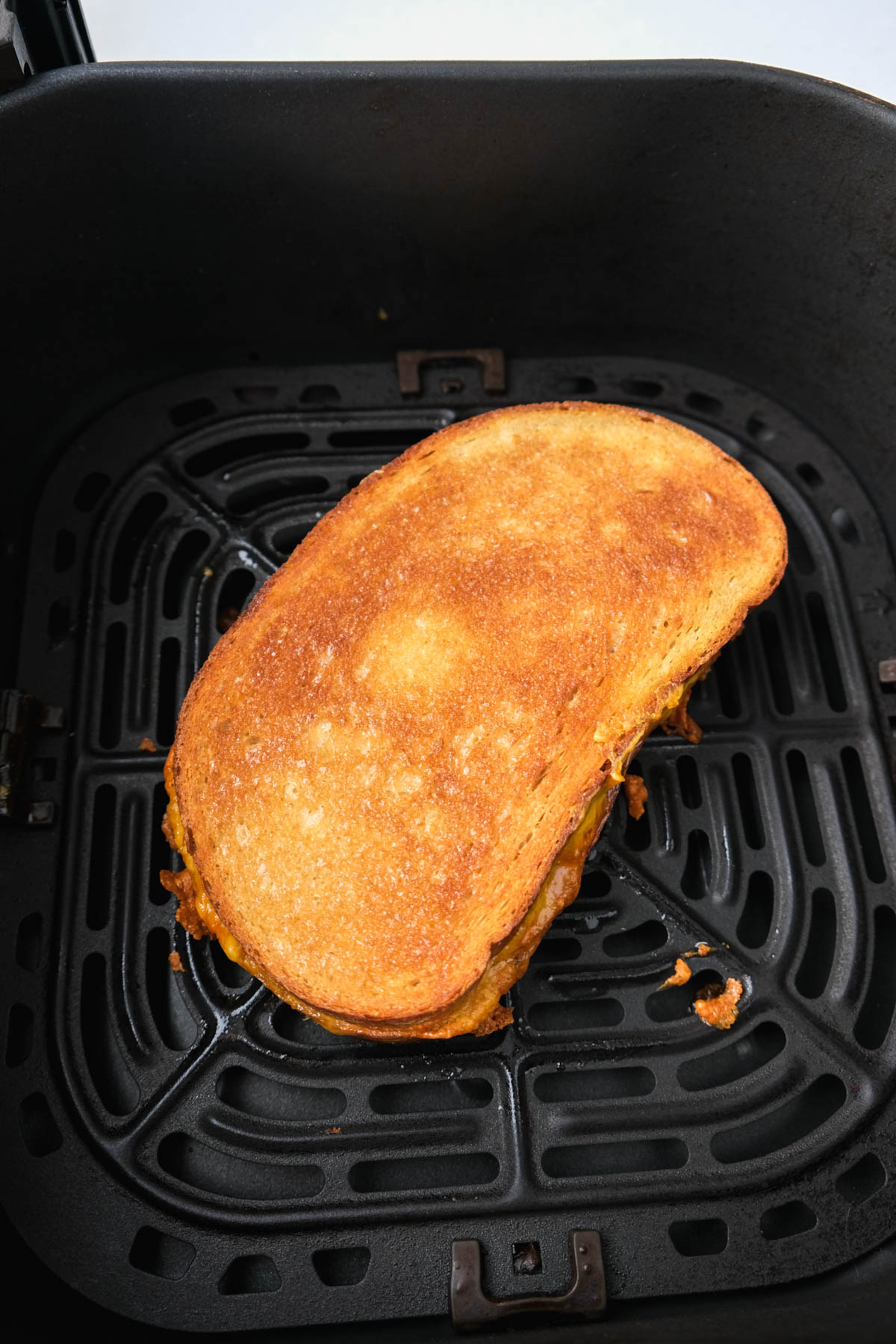 crispy brown outside of grilled ham and cheese sandwich sitting in black air fryer tray.