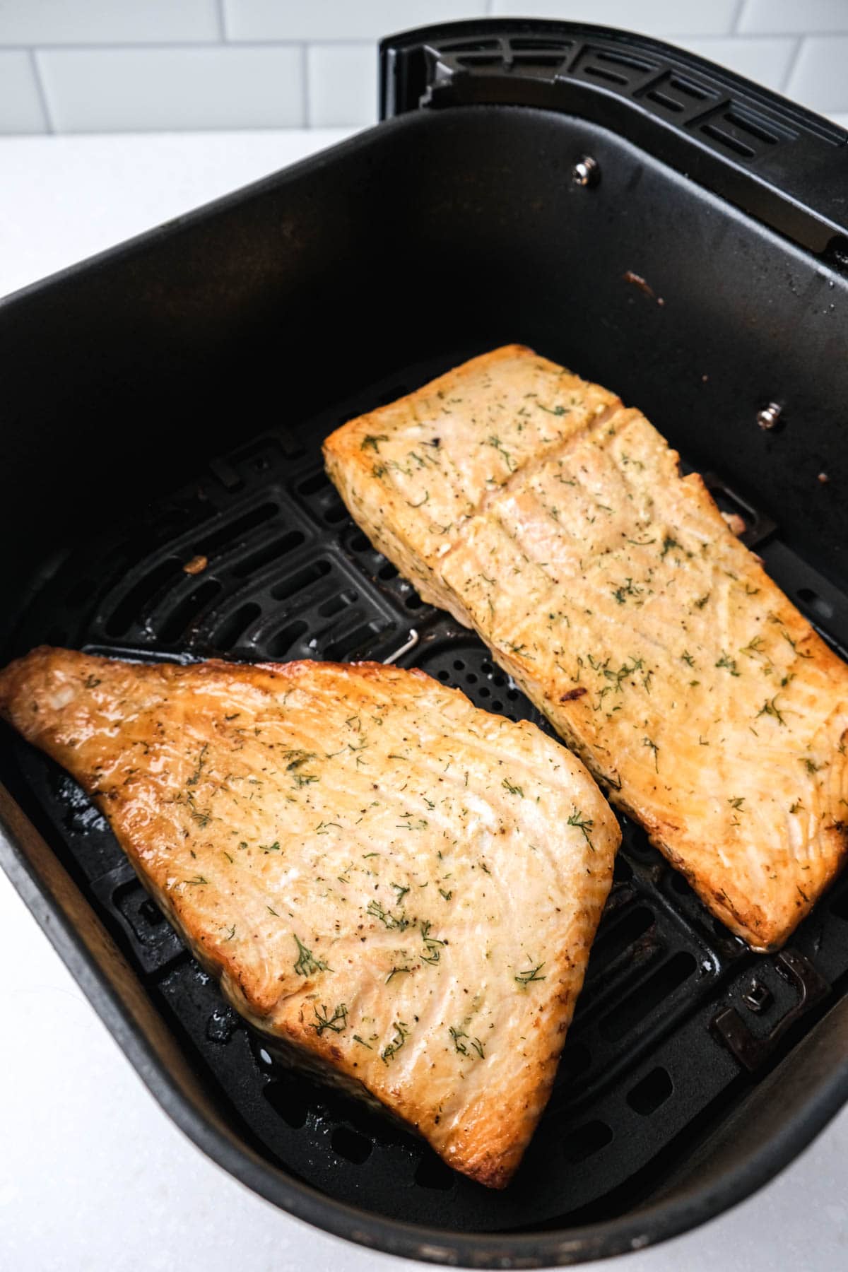 cooked salmon fillets in black air fryer tray on white counter top.
