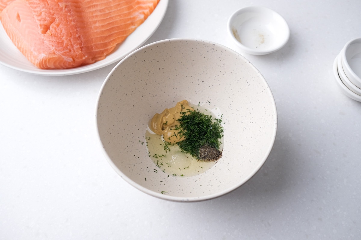 small white mixing bowl full of spices and mustard sitting on white counter top with raw salmon behind.