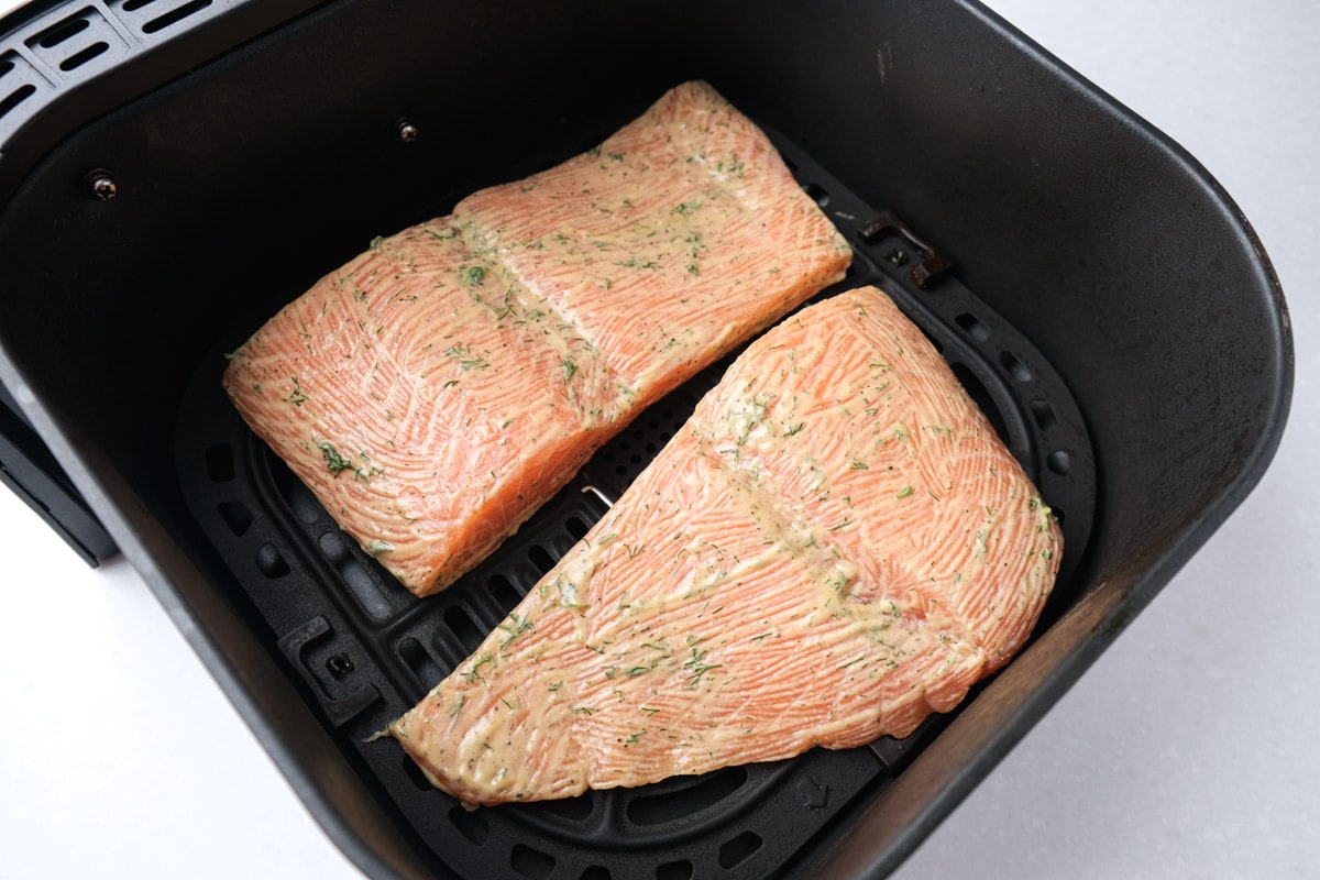 raw salmon fillets coated in marinade sitting in black air fryer basket on white counter top.