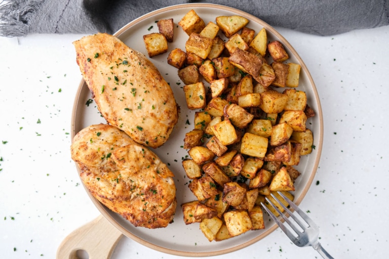 two cooked chicken breast and potatoes on white plate with silver fork on the edge.