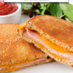 ham and cheese sandwich cut in half on plate with ketchup and lettuce and text overlay "ham & cheese in the air fryer".