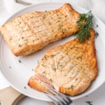 air fried salmon with fresh dill on top sitting on plate with fork in front.