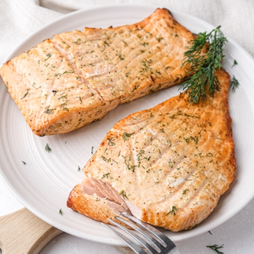 air fried salmon with fresh dill on top sitting on plate with fork in front.