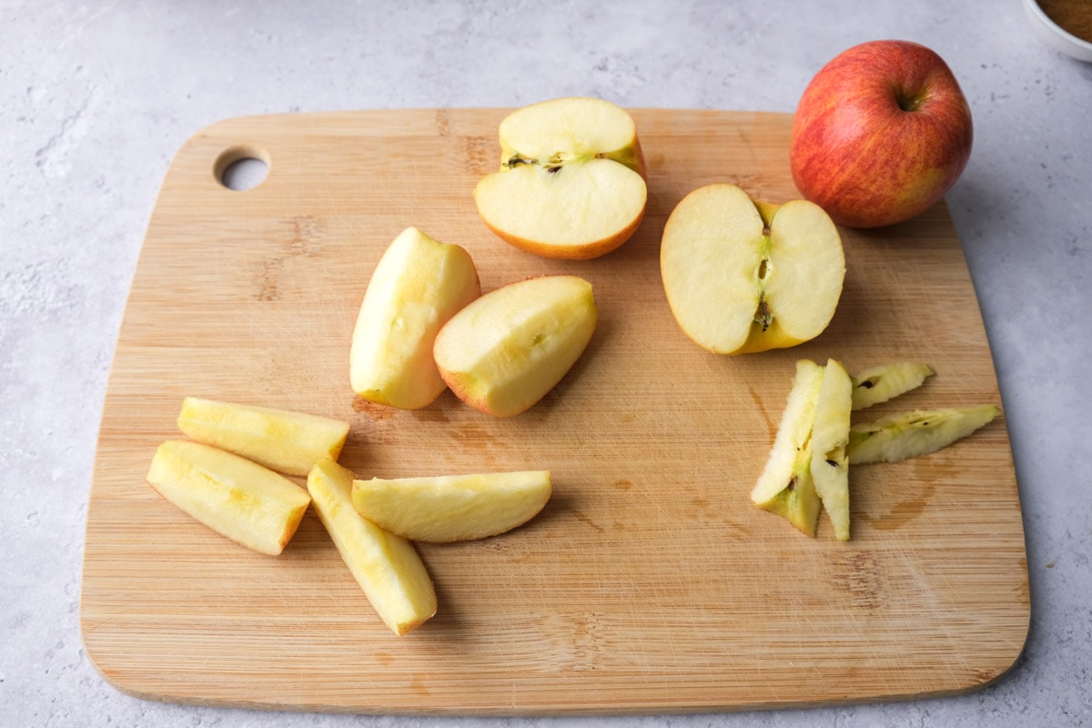 apple slices on wooden cutting board with whole red apple sitting beside.