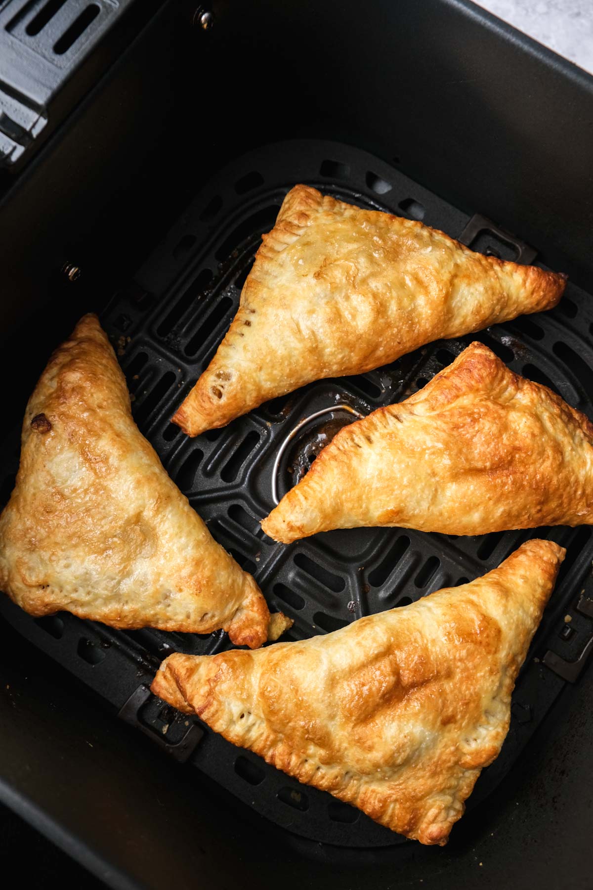 baked apple turnovers sitting in black air fryer tray.