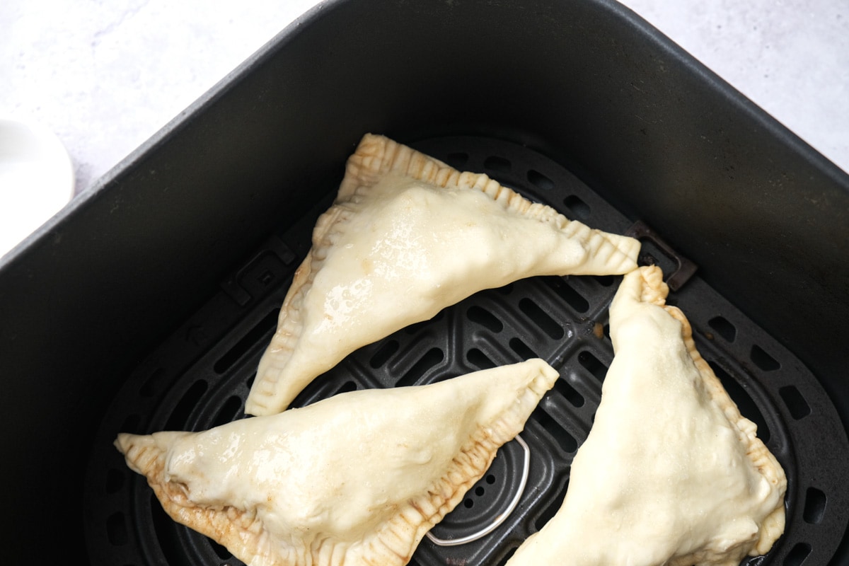 raw apple turnovers in black air fryer tray on counter.