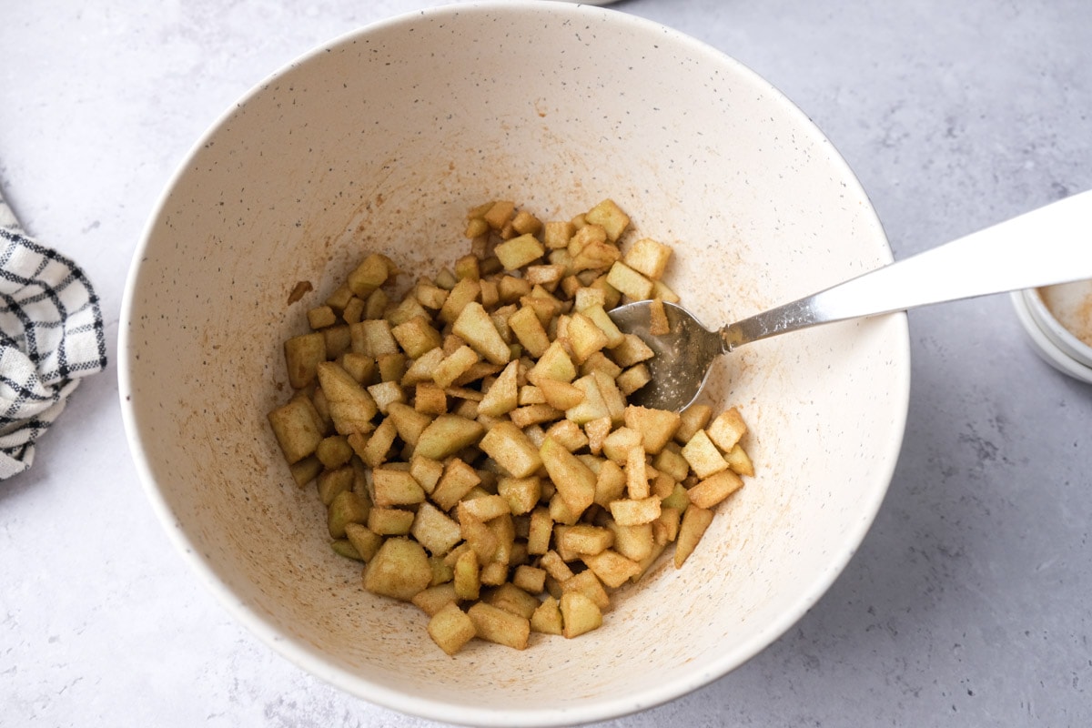 pieces of apple mixed in spices sitting in mixing bowl with silver spoon sticking out.