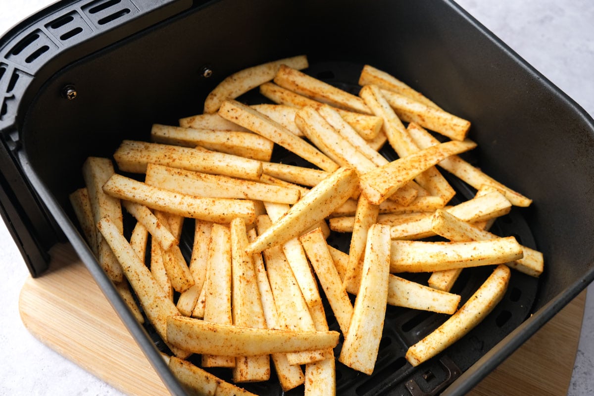 raw parsnip fries in black air fryer tray on grey counter.