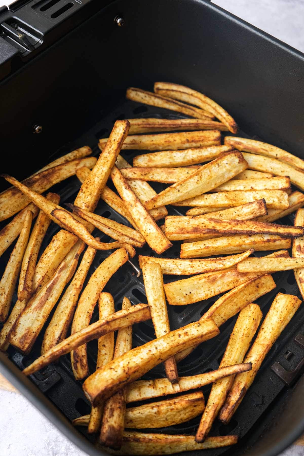 cooked parsnip fries in black air fryer basket.