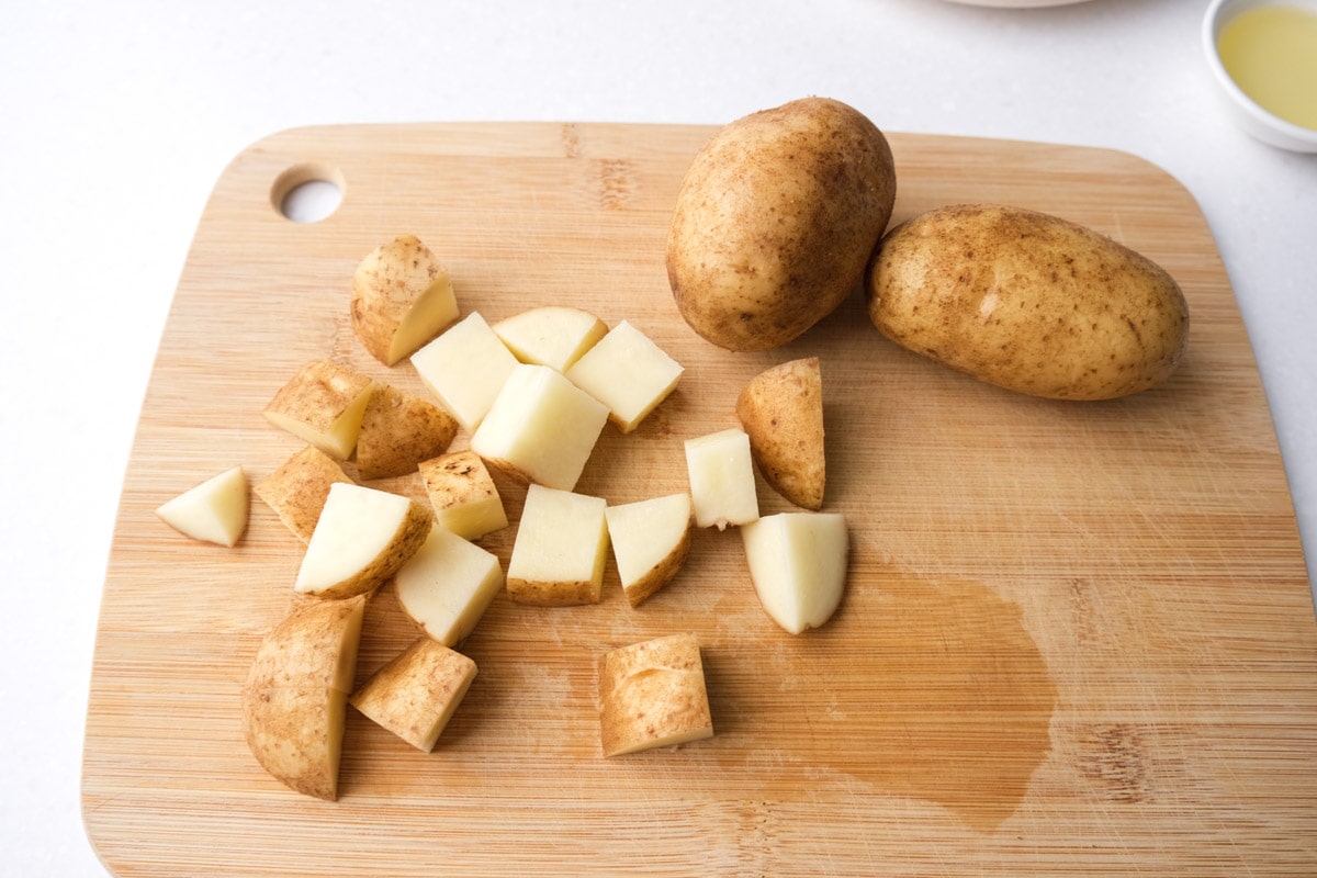diced cubes of potatoes beside larger potato on wooden cutting board.