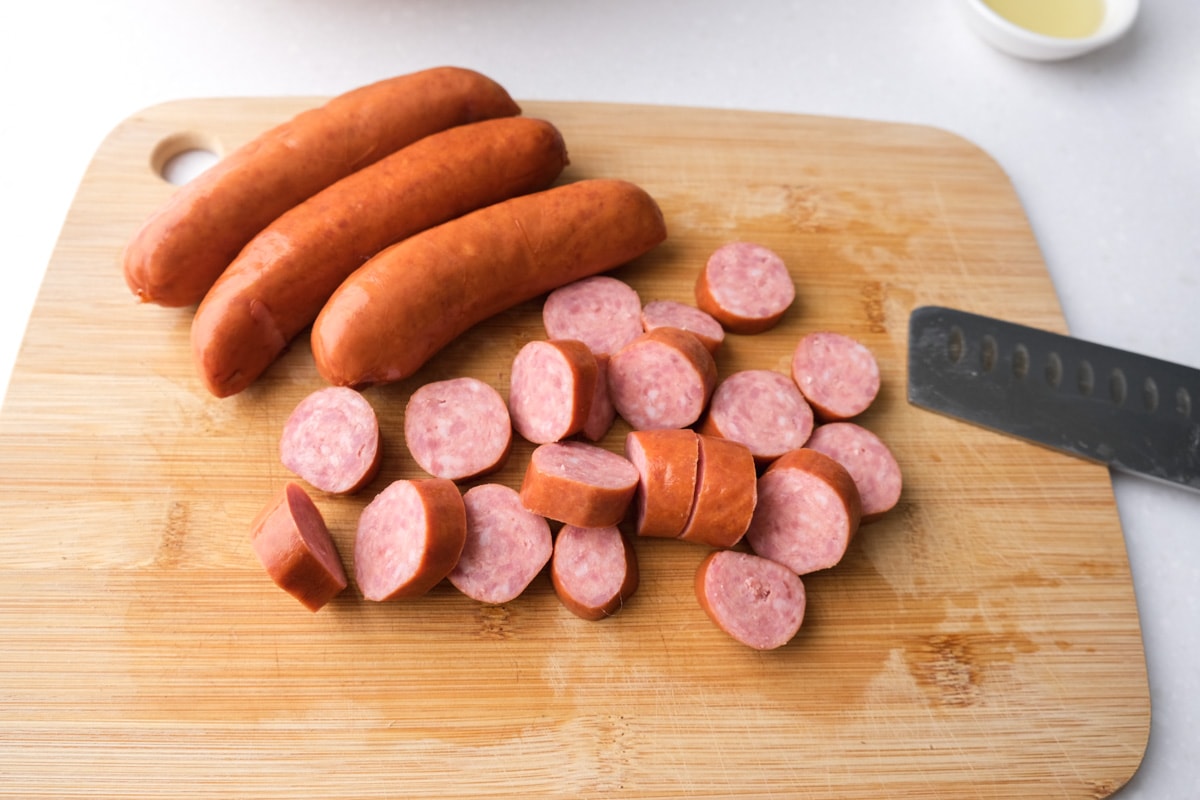pieces of sausages cut on wooden cutting board with whole sausages and knife beside.