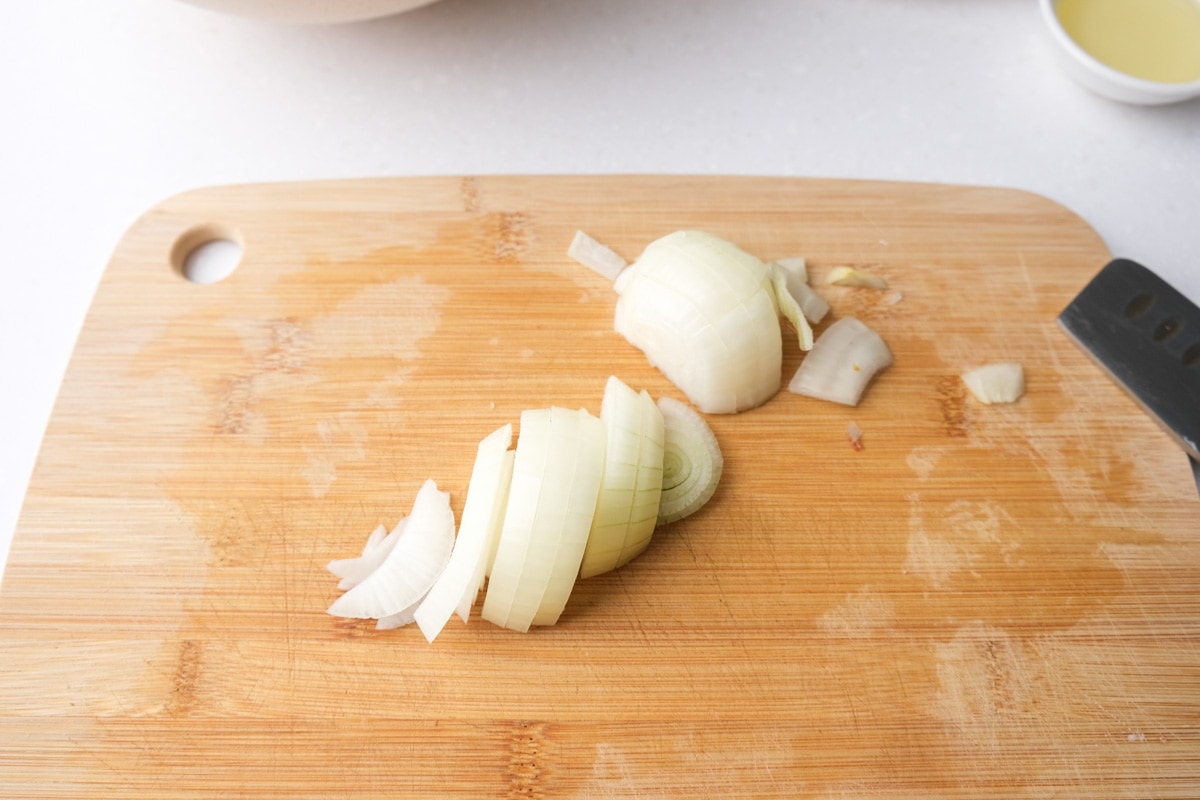 pieces of white onion sliced on wooden cutting board.