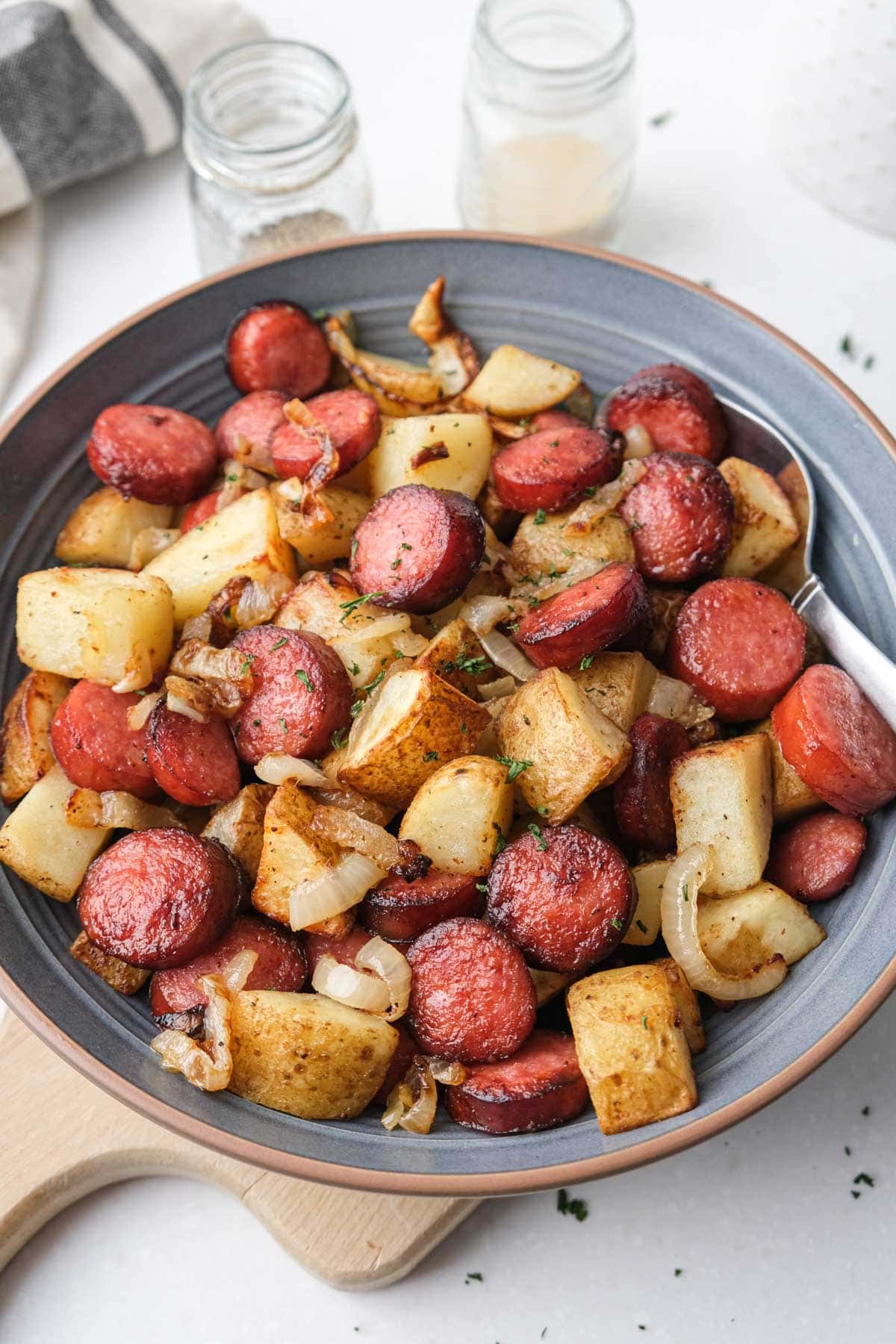 cooked potato pieces with sausage pieces and onions in blue bowl with white counter around.