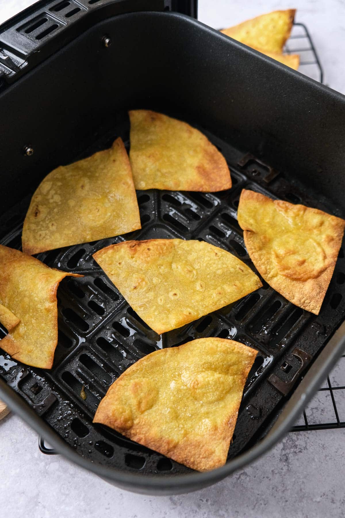 crispy tortilla chips in black air fryer basket sitting on counter.