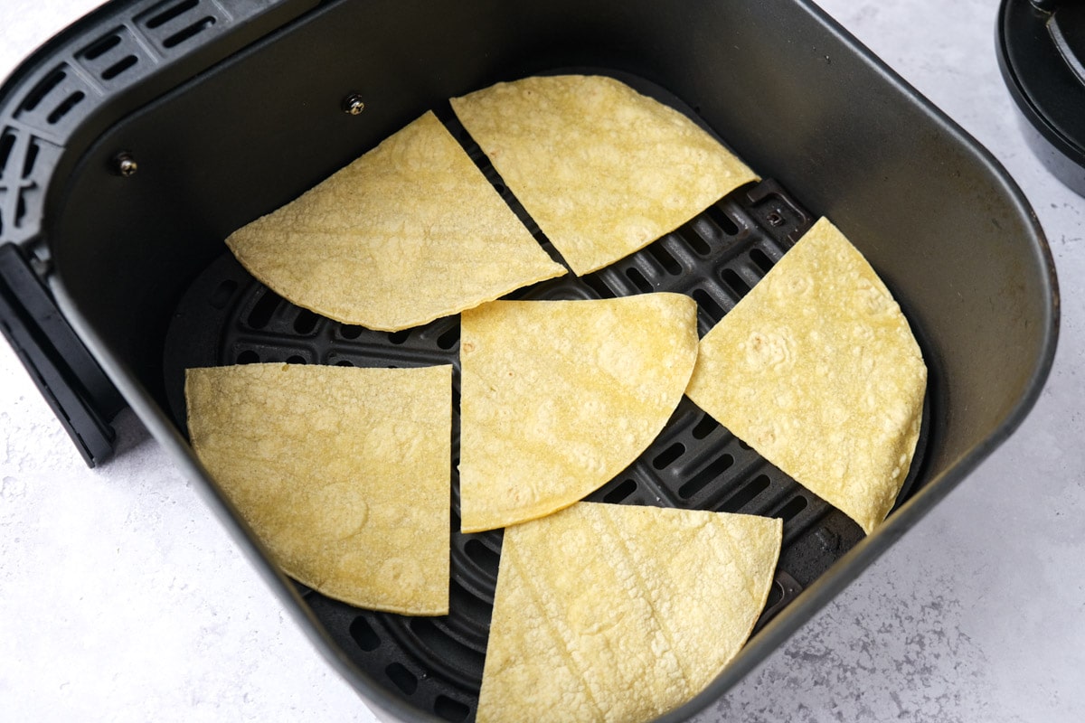 raw corn tortilla chips arranged flat in black air fryer tray.