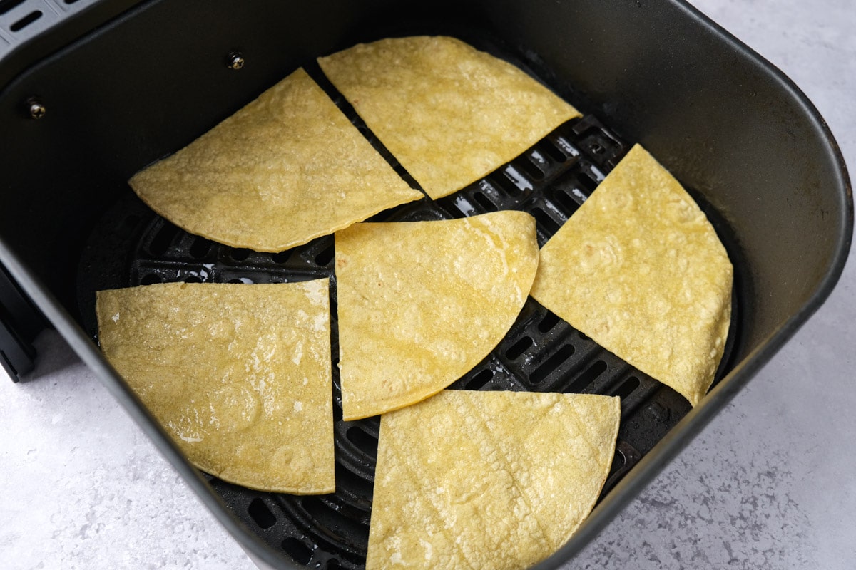 oily tortilla chips in air fryer basket on counter.