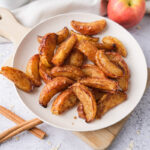plate full of baked apple slices covered in cinnamon.