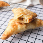 two apple turnovers on cooling rack one with bite out of it.