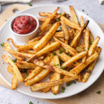 white plate covered in parsnip fries with ketchup for dipping