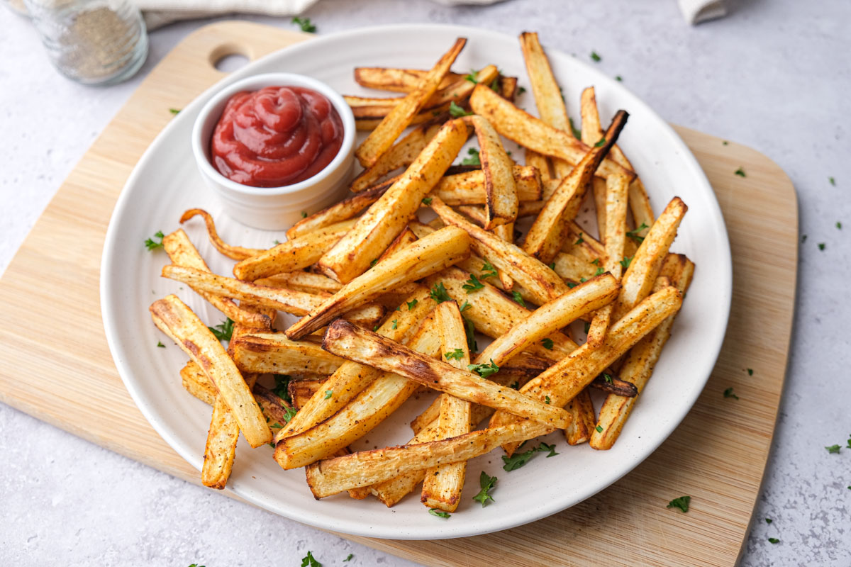 white plate covered in parsnip fries with ketchup for dipping