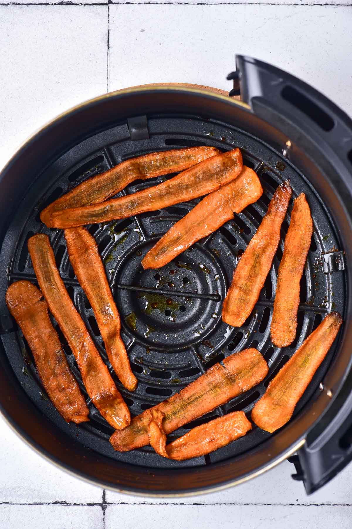 air fryer carrot strips in round black air fryer basket on white counter.