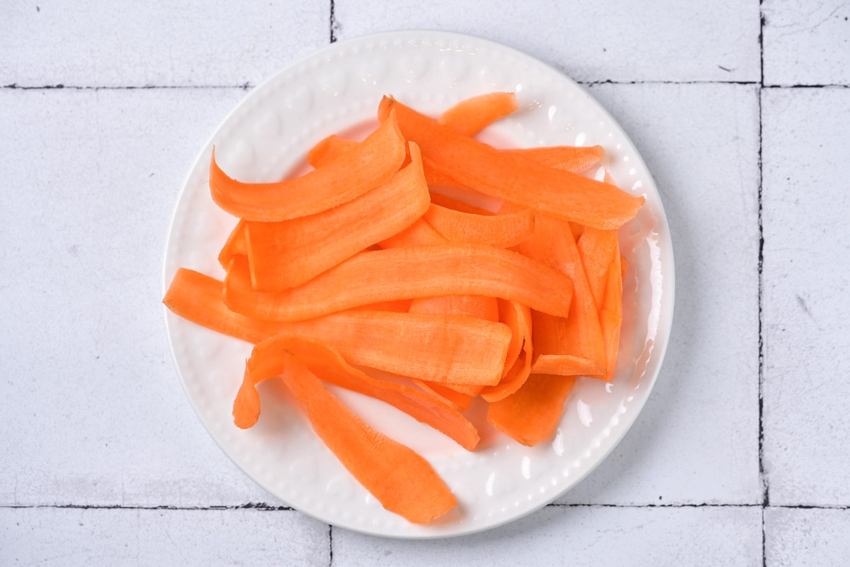 strips of raw carrots on white plate sitting on white tile counter.