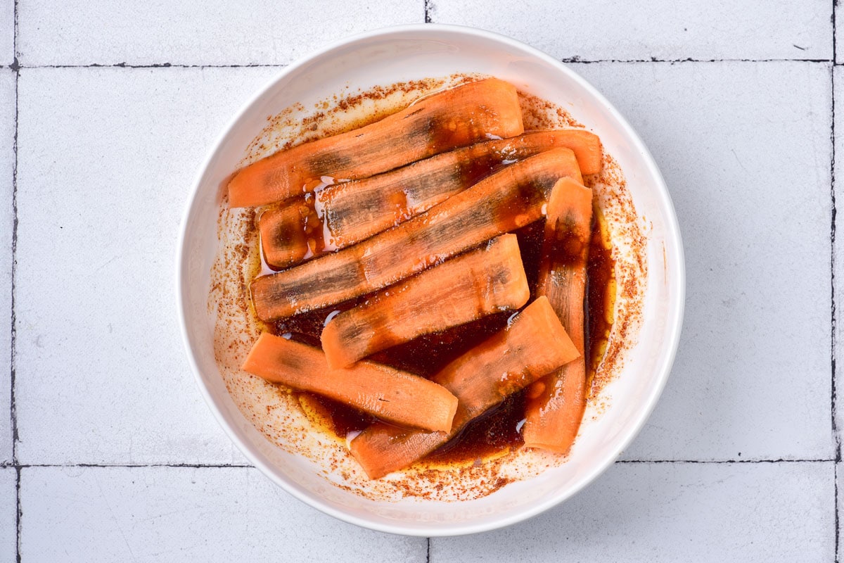 thin slices of raw carrot in white bowl of marinade.